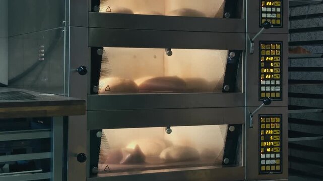 Fresh bread baking inside a professional bakery oven. Golden loaves rise and cook in a commercial kitchen, showing traditional baking process and artisan bread production