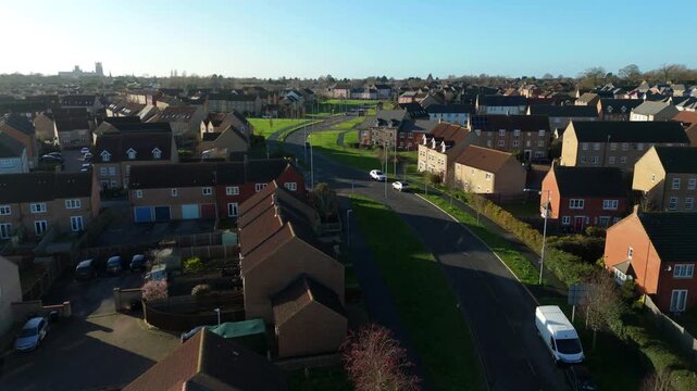 Drone view of a peaceful residential neighborhood in Ely Cambridgeshire showing rows of suburban houses and green gardens glowing under a warm UK golden hour sunset