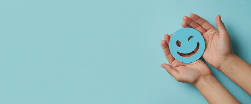 Woman hands holding blue paper cut smile face, positive thinking, mental health, and happy concept on blue background