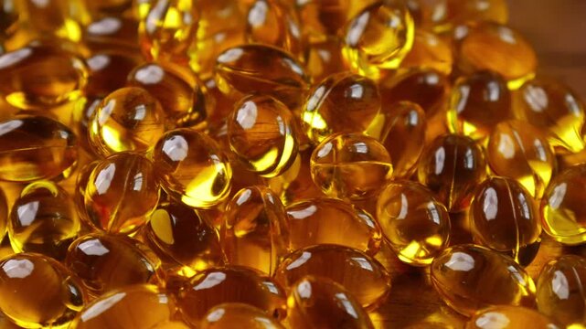 Golden yellow fish oil omega-3 supplement softgel capsules piled on wooden plate, health nutrition vitamin dietary supplement concept