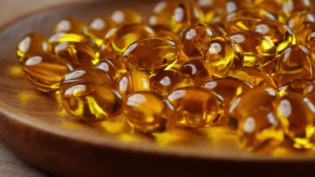 softgel capsules pouring out of opened glass bottle onto wooden plate, supplement herbal extract health concept