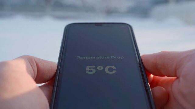 Hands holding smartphone showing smooth temperature drop close-up on blurred background