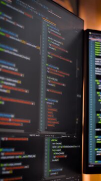 Vertical video close up computer monitors displaying fictional programming code and software development interface, technology workspace concept