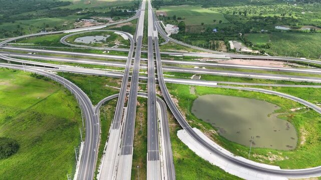 Aerial view of modern highway interchange with multilayer roads and curved ramps surrounded by green farmland, showcasing transportation infrastructure, urban development, and road network planning.