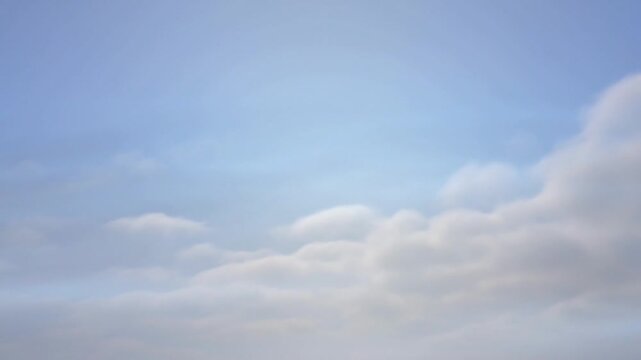 Serene daytime sky with soft white clouds against a clear blue background, viewed from below with a sense of calmness.