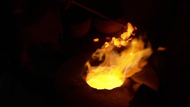 Close up of molten metal bubbling in a glowing crucible with bright orange flames and sparks flying