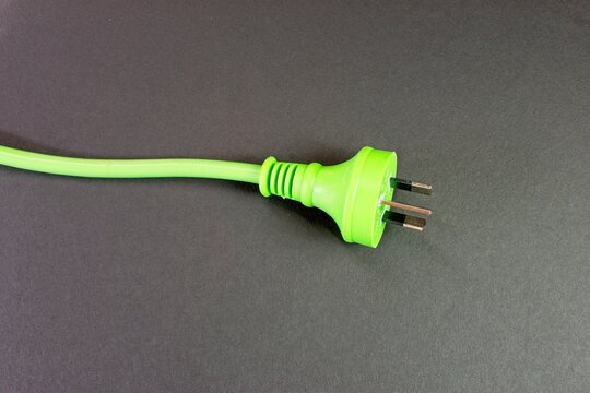 Closeup of a green Australian electricity cord plug socket on a black background. This electrical power cable illustrates the concept of expensive energy and bill cost savings.