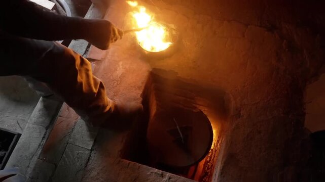 High angle shot of a blacksmith opening a floor furnace lid and stoking a small crucible with glowing flames