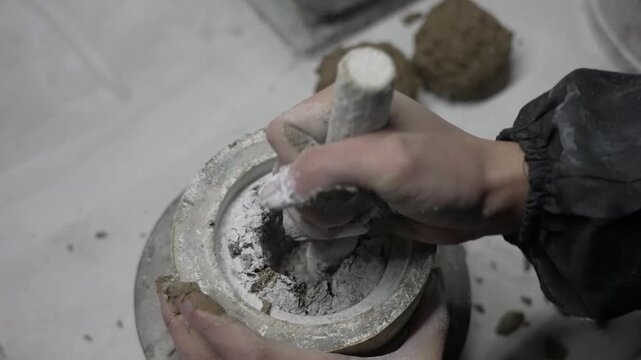Close up of an artist using a stone pestle to pack and mold a clay mixture into a circular ceramic mold with white powder