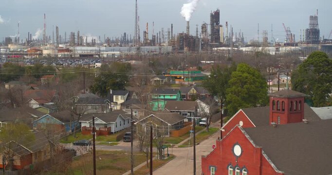 Drone reveal shot pulling back from a residential neighborhood to show chemical plant smokestacks near Baytown, Texas
