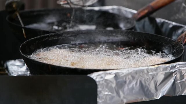 High-angle shot of breaded chicken chunks deep frying in a traditional wok. The hot oil is bubbling intensely with steam rising, showing the fast-paced cooking process in a professional kitchen.
