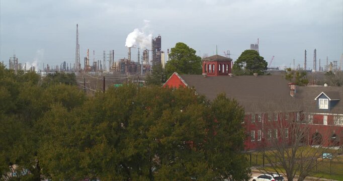 Drone reveal shot pulling back from a residential neighborhood to show chemical plant smokestacks near Baytown, Texas