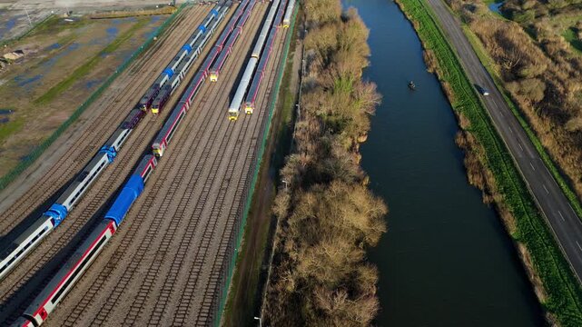 Aerial view of a railway yard with train carriages parked next to a river and road with moving cars in Ely UK during golden hour