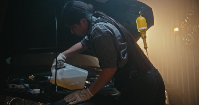 Professional Woman Auto Technician Refills Automotive Fluid Under Hood in Modern Workshop. Wearing Protective Gloves, Young Female Performs Routine Car Service With Confidence and Technical Expertise.