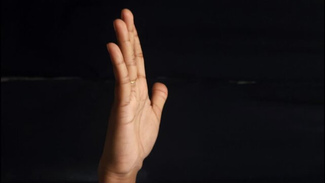 Close-up of a human hand showing different gestures against a black background. The isolated composition highlights communication, body language, and symbolic meaning of hand signs. Ideal for concepts