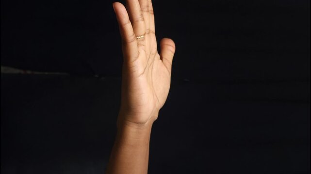 Close-up of a human hand showing different gestures against a black background. The isolated composition highlights communication, body language, and symbolic meaning of hand signs. Ideal for concepts