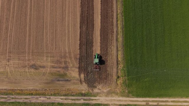 Tractor plowing field from above: A green tractor cultivates a rich brown soil in a vast agricultural field, showcasing the process of farming from a bird's eye view.
