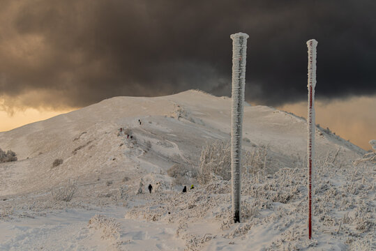 Dramatic winter view of Smerek peak in Bieszczady Mountains illuminated by golden sunlight against dark stormy clouds.