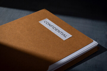 Brown manila folder with a CONFIDENTIAL label on a dark surface. Corporate secrecy, data privacy,...