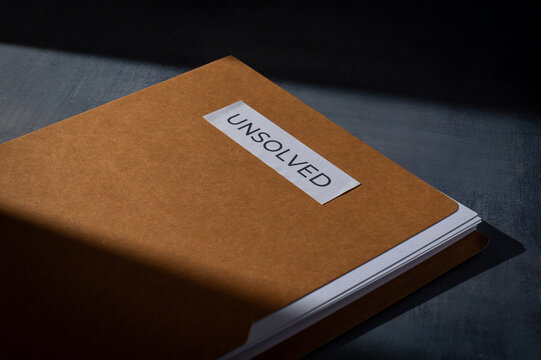 Brown manila folder with UNSOLVED label on a dark surface. Mystery, cold cases, criminal investigation, and unresolved problems concept.
