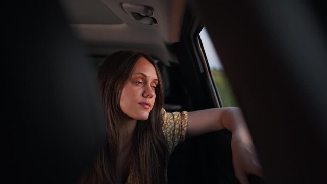 Woman talks to passenger inside car during trip. Female driver converses with person in vehicle. Girl speaks while sitting in automobile. Woman having conversation during drive. Female talks.