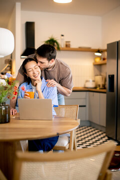 Couple shares a moment in kitchen while working on a laptop and enjoying a drink