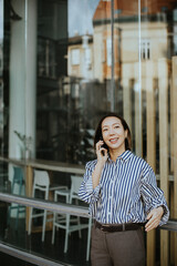 Fototapeta premium Korean woman talks on the phone outside a modern building in the afternoon sun