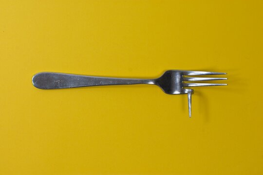 Closeup of a broken and bent silver cutlery fork on a yellow background. The bent fork illustrates the concept of inefficiency, harm, danger, useless products and enshitification.