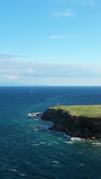 Scenic view of a rocky coastline with clear blue sea and sailboats under a bright sky near Koroni, Greece. Peaceful seascape ideal for travel and nature concepts.