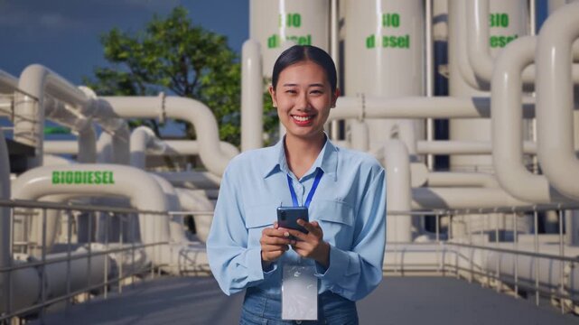 Asian Female With Her Smarphone at Biodiesel Production Facility, She Is Looking At The Camera With A Smile