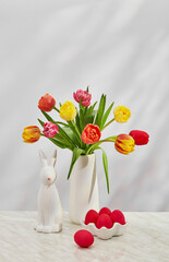 Tulips in vase with bunny and red eggs on marble surface