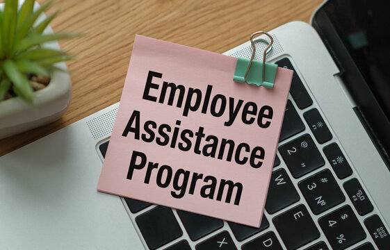 A top-down close-up shot of a pink square sticky note with the words Employee Assistance Program in bold black font.