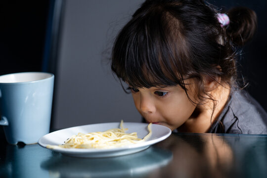 Cute childhood emotion during eating. Kid eating spaghetti meal at home. Messy spaghetti mouth and lips moment. Portrait of toddler eating pasta indoors. Cute girl slurping noodles during dinner.