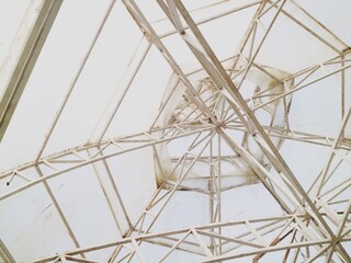 Obraz premium Intricate network of beige metal beams and supports under a transparent roof with a clear blue sky visible