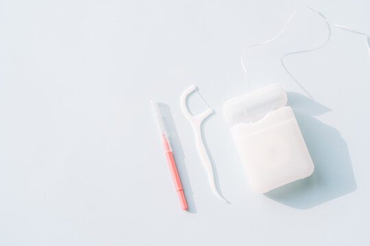 Interdental brush, floss pick and dental floss container on light blue background, oral care routine set.