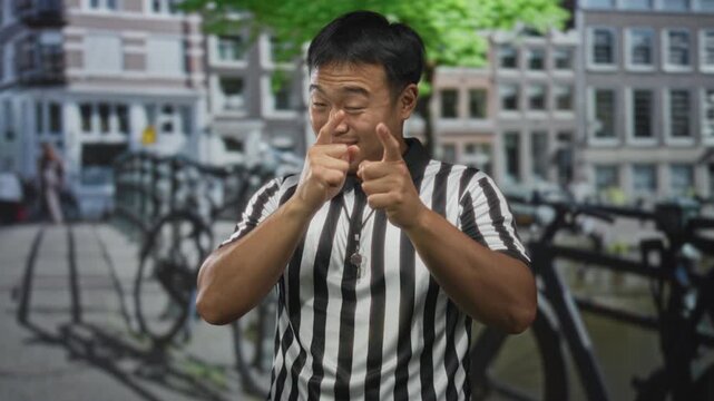Man in black and white referee shirt with whistle around neck points both index fingers toward camera on street; joy.