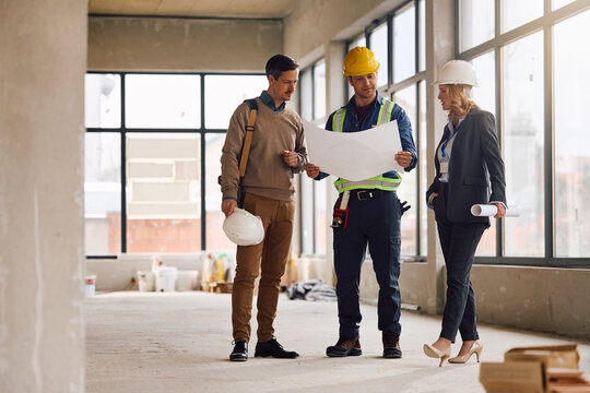 Building site foreman analyzing blueprints with project managers at construction site.