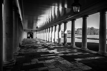 Naklejka premium Visitors walk through the corridor of Greenwich Queens House in London. The building features classic architecture and a well-maintained path. Sunlight creates shadows on the ground.