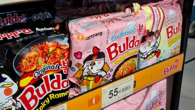 Assorted Samyang Buldak carbonara and original flavor spicy ramen instant noodle packets on supermarket retail display shelf for South Korean food on March 18, 2026 in Bangkok, Thailand