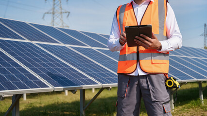 solar panel installation, A technician stands near solar panels, The worker uses a digital tablet, A specialist monitors the system, Data is checked on a screen, Maintenance is performed outdoors © Jakub