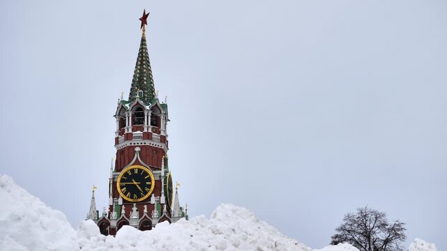 Spasskaya Tower clock face rising above large snowdrifts with a cloudy sky