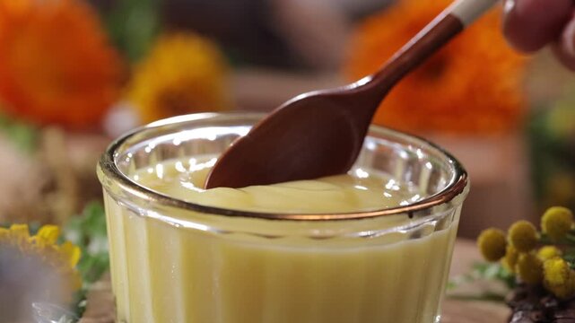 The image of royal jelly dripping into a glass bowl with a spoon is placed against a natural background