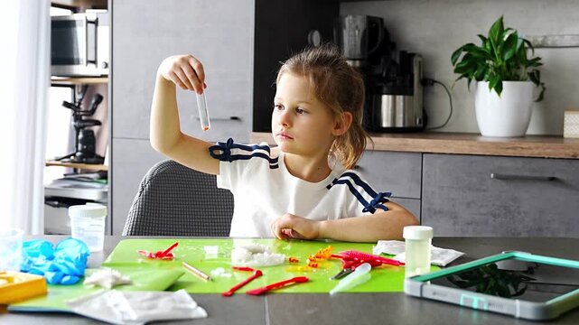 Young girl holding test tube with small crystal and carefully examining experiment result at home laboratory table. Scientific observation, practical STEM learning through crystal growing experiment.