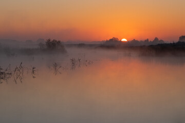 Fototapeta premium A beautiful, misty morning by the quiet river with trees reflecting in the calm water