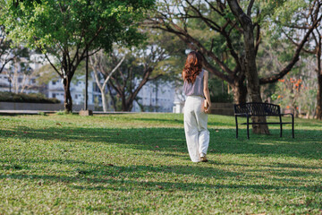 Fototapeta premium Young woman walking away in green park exploring nature