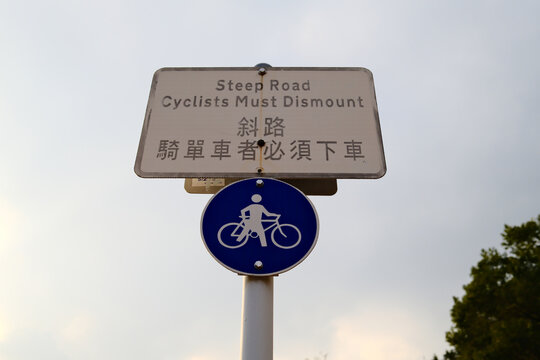 Steep road cyclists must dismount bilingual warning sign with bicycle symbol on pole in Hong Kong