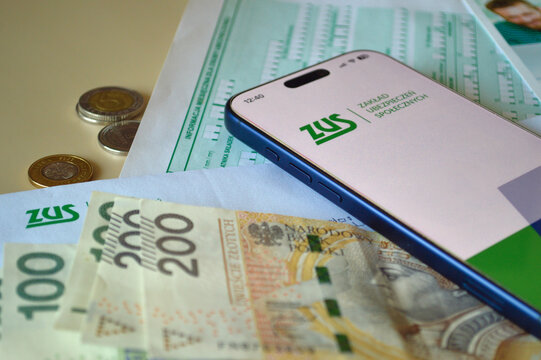 Smartphone displaying the ZUS logo resting on Polish zloty banknotes and official social insurance documents on a bright desk representing digital finance and government services in Poland.