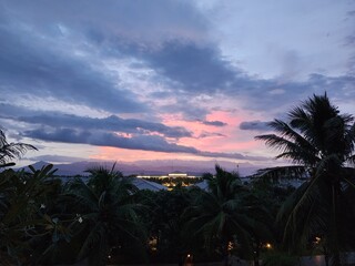Obraz premium Tropical Sunset with Pink Clouds and Palm Tree Silhouettes over Mountain Range 산맥 위로 펼쳐진 분홍빛 노을 구름과 야자수 실루엣의 열대 풍경