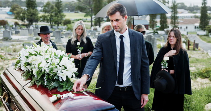 Man, funeral and rose with offering on coffin for grief or mourning death together in graveyard. Male person, sad family and empathy with flower for farewell, burial or paying respect in cemetery