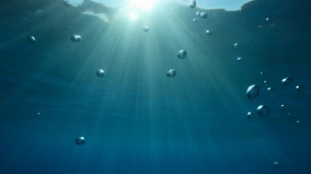 Sunlight rays penetrate the deep blue ocean water as air bubbles rise toward the surface.